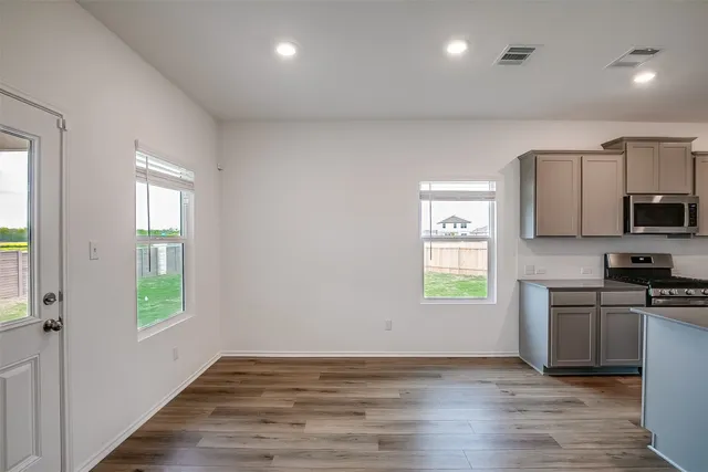a view of a kitchen and an empty room with wooden floor and windows