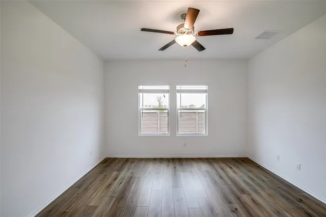 an empty room with wooden floor ceiling fan and window
