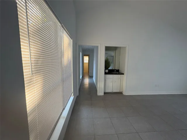 a view of a hallway to an empty room with wooden floor and a kitchen