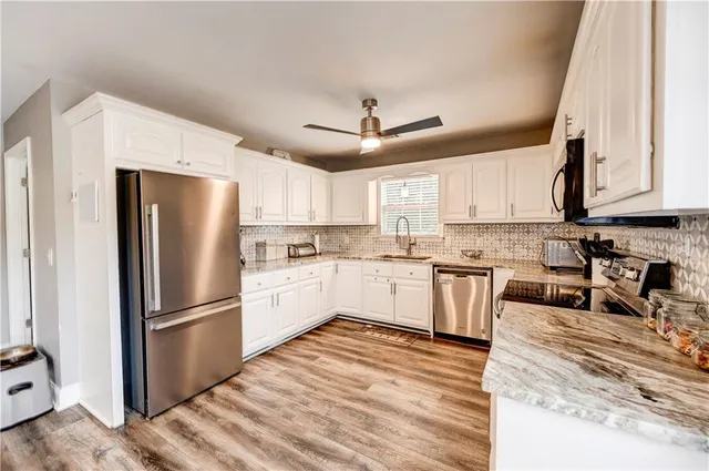 a kitchen with stainless steel appliances granite countertop a refrigerator a stove a sink and white cabinets with wooden floor