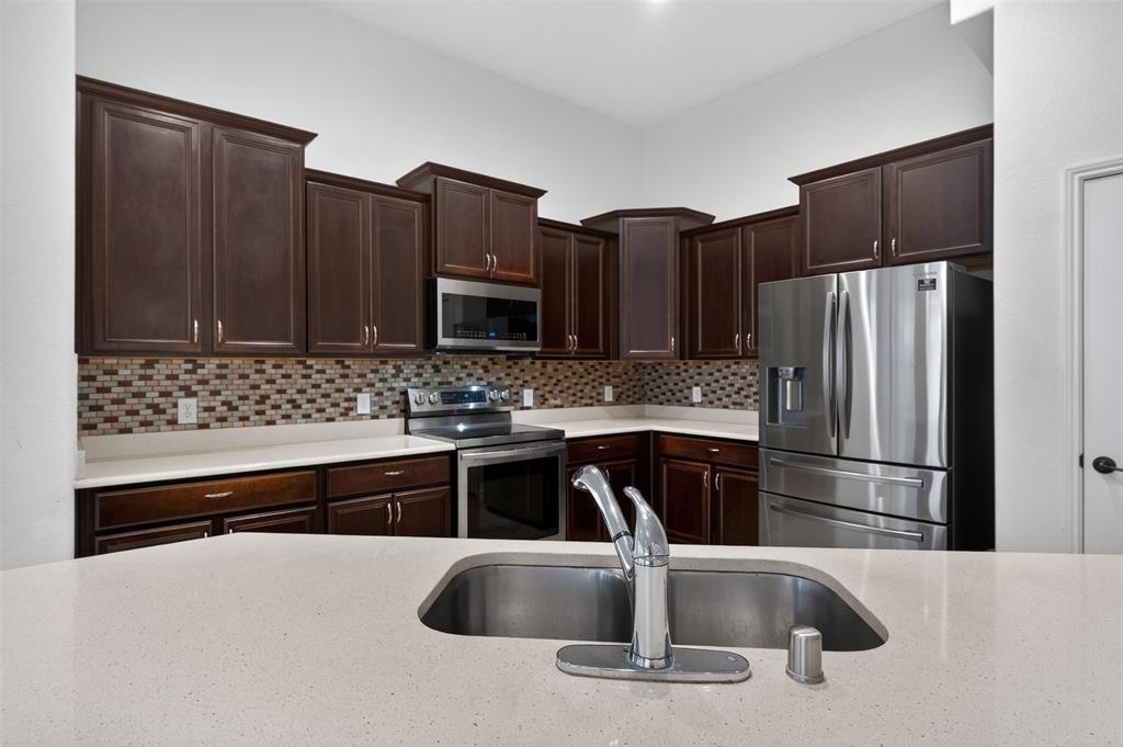 8728 Maple Ridge Trail Fort Worth, TX 76244 - Photo 15 of 40 Kitchen featuring dark wood cabinetry, stainless steel appliances, mosaic tile backsplash, and light-toned countertops