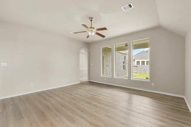 a view of an empty room with wooden floor and a ceiling fan