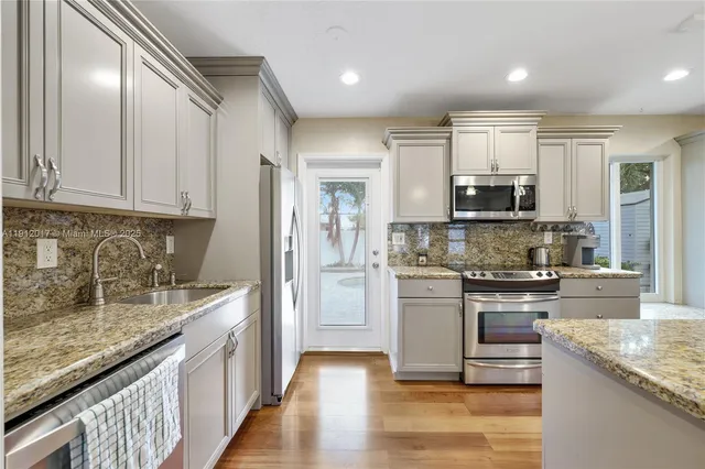 a kitchen with kitchen island granite countertop a stove top oven a sink and dishwasher a refrigerator with wooden floor