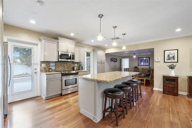 a kitchen with stainless steel appliances granite countertop a stove top oven a refrigerator a sink dishwasher and a dining table with wooden floor