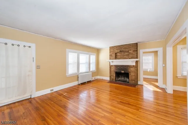 an empty room with wooden floor fireplace and windows