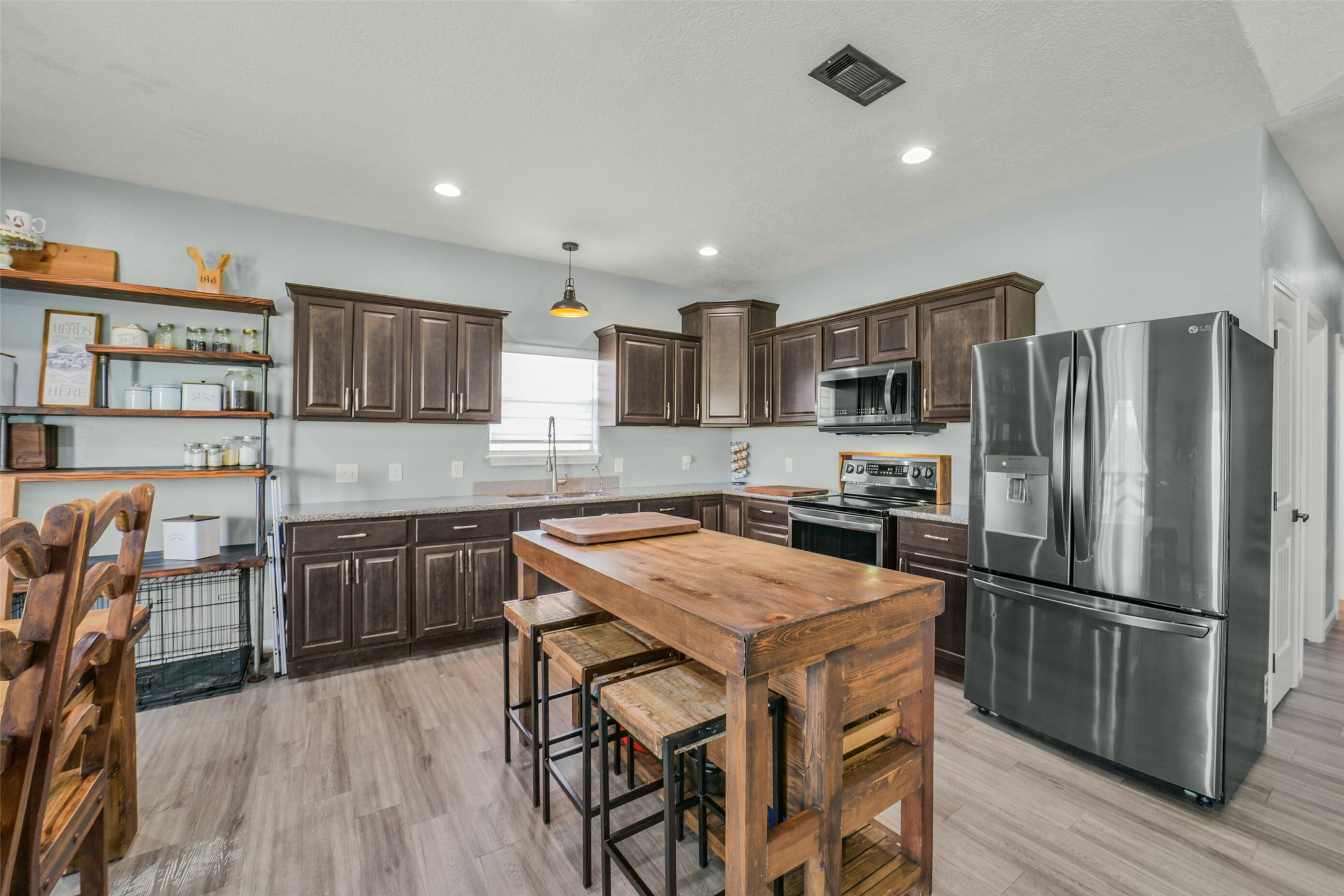 11301 South FM 441 Road El Campo, TX 77437 - Photo 11 of 43 This kitchen features modern stainless steel appliances, dark wood cabinetry, and an island with rustic wooden stools. It includes open shelving for added storage and a dining area.