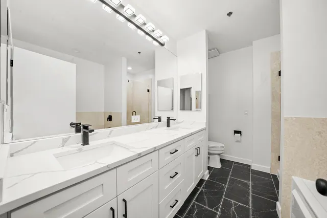 a bathroom with a double vanity sink and mirror with toilet