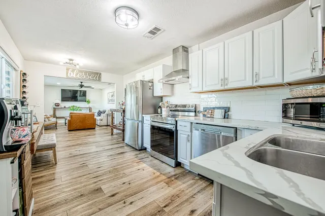 a kitchen with stainless steel appliances granite countertop a refrigerator a stove top oven a sink dishwasher and white cabinets with wooden floor