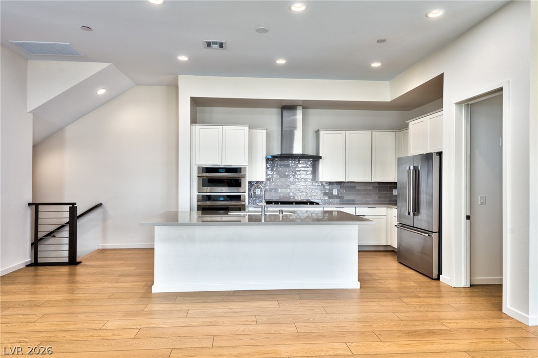 3327 Esker Rdg Avenue Henderson, NV 89044 - Photo 3 of 24 A contemporary kitchen features a spacious island and integrated appliances, complementing the rich hardwood flooring and sleek cabinetry.