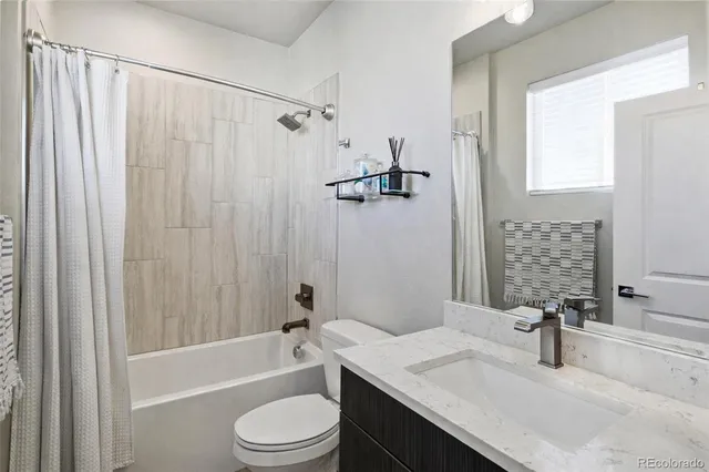 a bathroom with a granite countertop bathtub shower sink vanity mirror and toilet