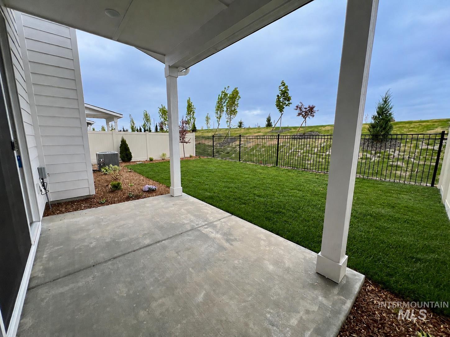 8098 West Fern Street Eagle, ID 83616 - Photo 2 of 22 Covered concrete patio with a manicured lawn, surrounding landscaping, and a black metal fence