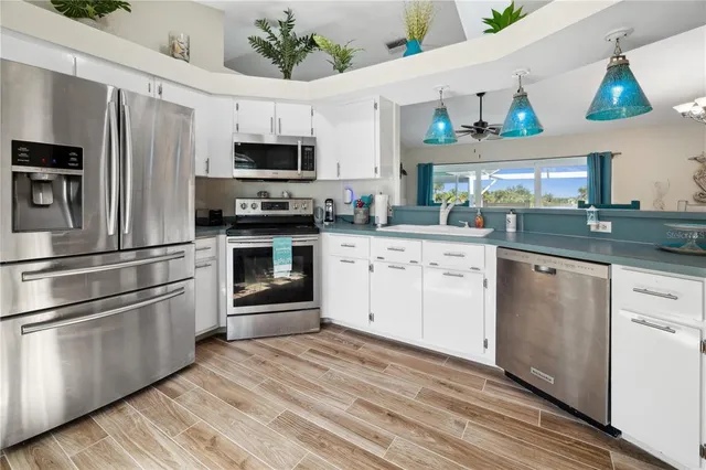 a kitchen with stainless steel appliances granite countertop a refrigerator oven a sink dishwasher and white cabinets with wooden floor