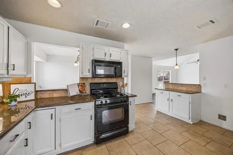 a kitchen with granite countertop white cabinets appliances and a counter top space