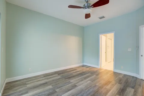 an empty room with wooden floor ceiling fan and windows