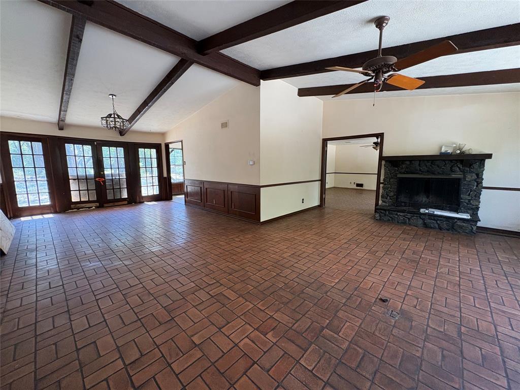 5454 Ranchero Lane Dallas, TX 75236 - Photo 5 of 24 Vaulted ceiling with exposed wood beams, brick-patterned flooring, wood wainscoting, stone-clad fireplace, and multiple sets of French doors
