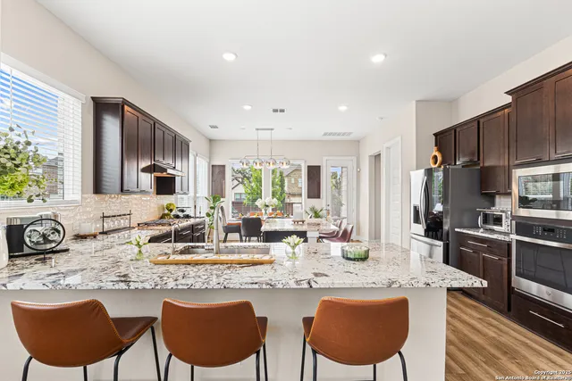 a kitchen with stainless steel appliances granite countertop a stove a sink a microwave a refrigerator and chairs