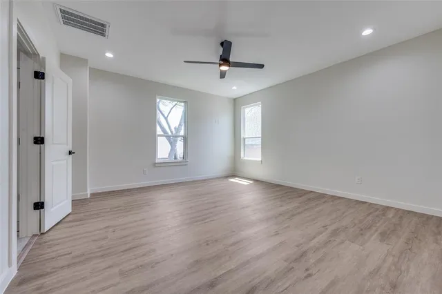an empty room with wooden floor ceiling fan and windows