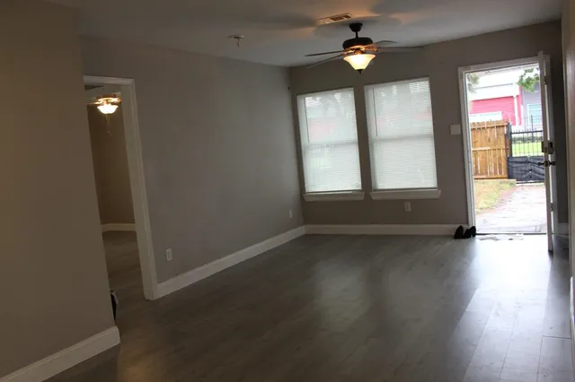 an empty room with wooden floor fan and windows
