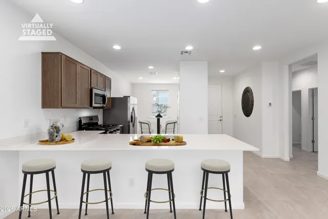 a kitchen with stainless steel appliances kitchen island granite countertop a dining table chairs and a refrigerator