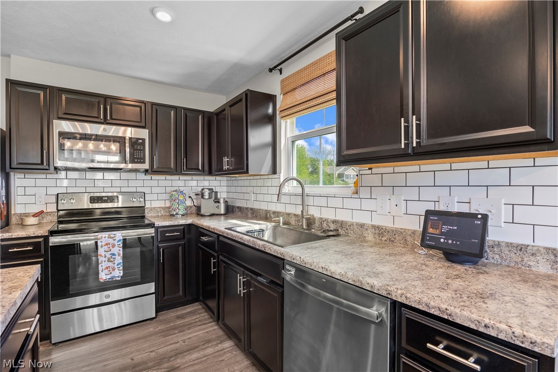 2161 Fowl Road Elyria, OH 44035 - Photo 5 of 46 Kitchen featuring dark wood cabinetry, stainless steel appliances, a subway tile backsplash, speckled countertops, and wood-finish flooring