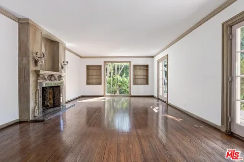 an empty room with wooden floor fireplace and windows