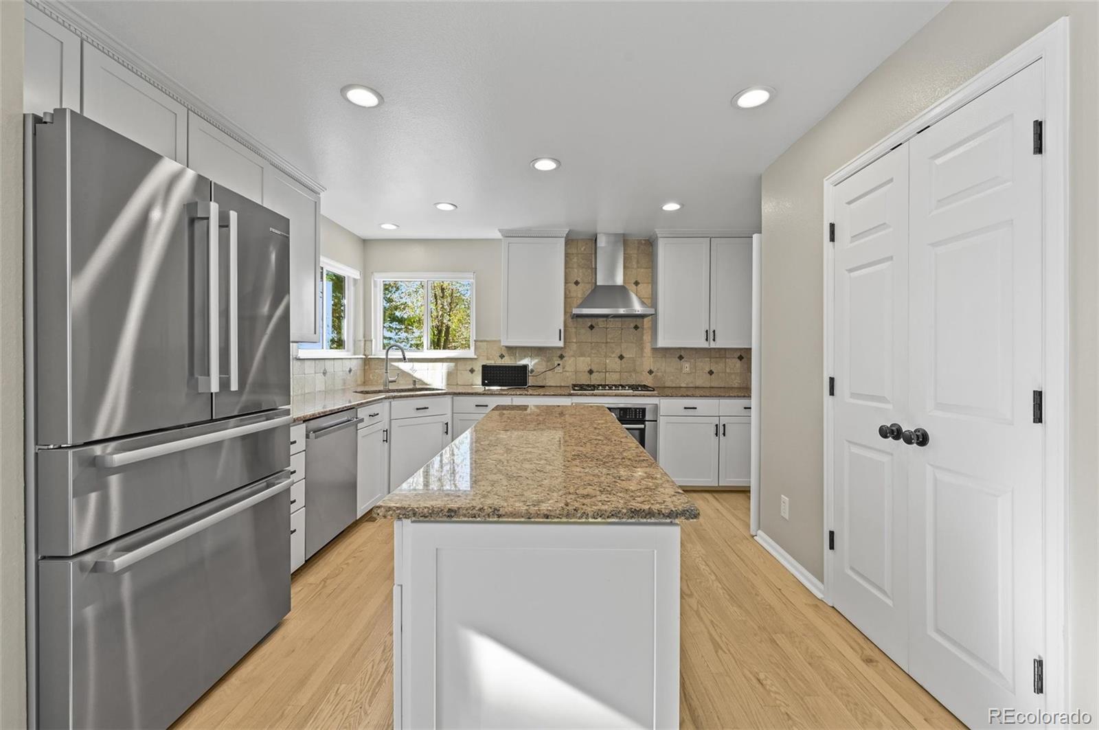 10096 Hughes Place Highlands Ranch, CO 80126 - Photo 7 of 50 a kitchen with kitchen island granite countertop stainless steel appliances a refrigerator cabinets and wooden floor
