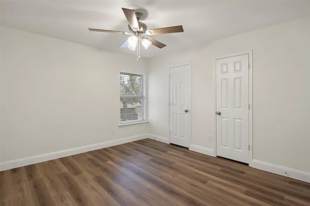 an empty room with wooden floor chandelier fan and windows