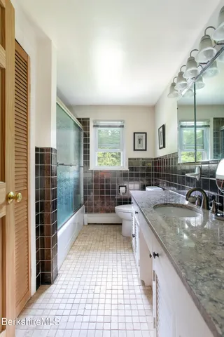 a bathroom with a granite countertop sink a toilet a mirror and shower