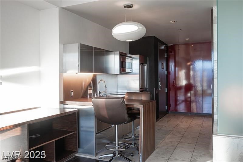 4381 West Flamingo Road, Unit 3303 Las Vegas, NV 89103 - Photo 10 of 37 Kitchen featuring a breakfast bar area, a sink, stainless steel microwave, modern cabinets, and pendant lighting