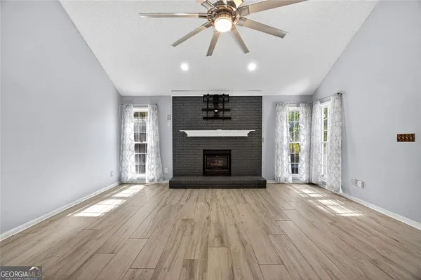 an empty room with windows a fireplace a ceiling fan and wooden floor