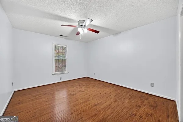 an empty room with wooden floor chandelier fan and windows