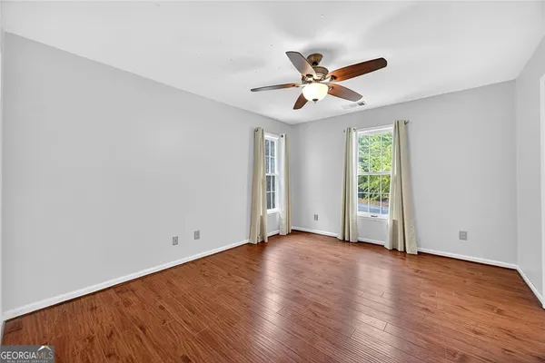 an empty room with wooden floor fan and windows