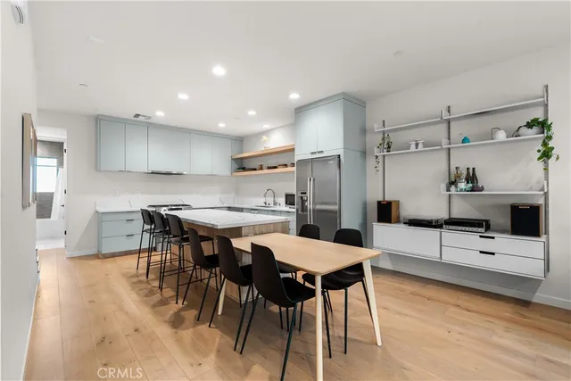 a kitchen with stainless steel appliances kitchen island granite countertop a dining table chairs and a refrigerator