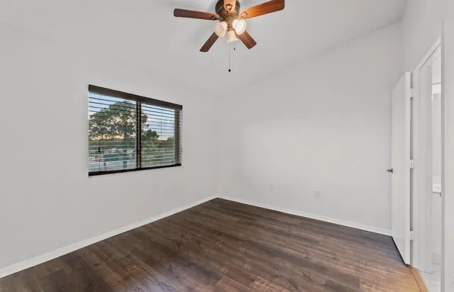 an empty room with wooden floor ceiling fan and window