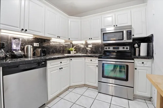 a kitchen with stainless steel appliances granite countertop a sink a stove top oven and white cabinets