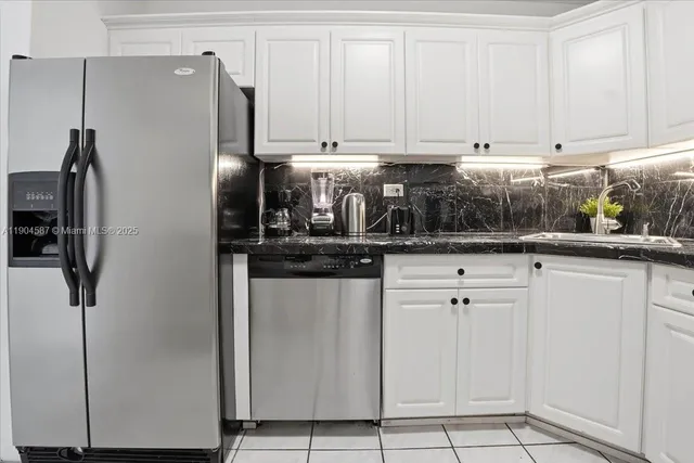 a kitchen with stainless steel appliances granite countertop a refrigerator a sink and white cabinets