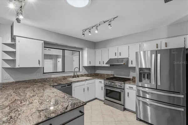 a kitchen with stainless steel appliances granite countertop a stove a sink dishwasher a refrigerator and white cabinets with wooden floor