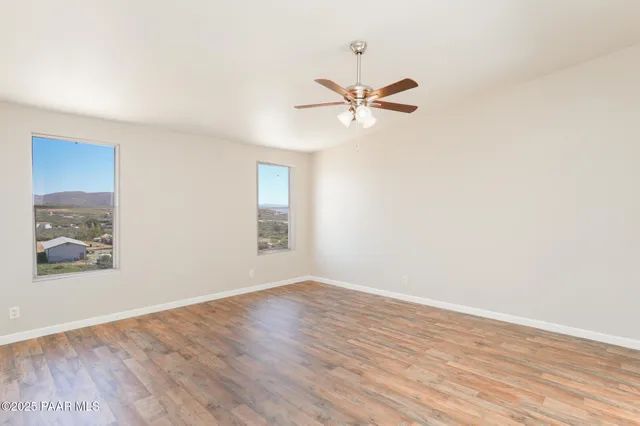 an empty room with wooden floor fan and windows