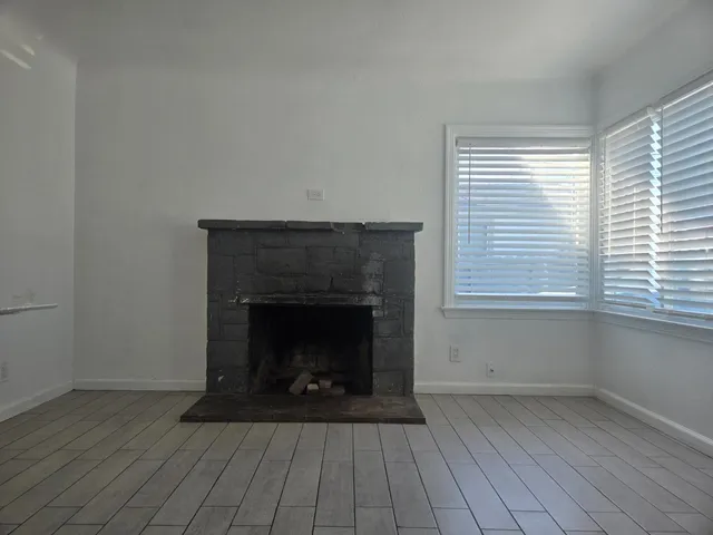 an empty room with wooden floor a fireplace and windows