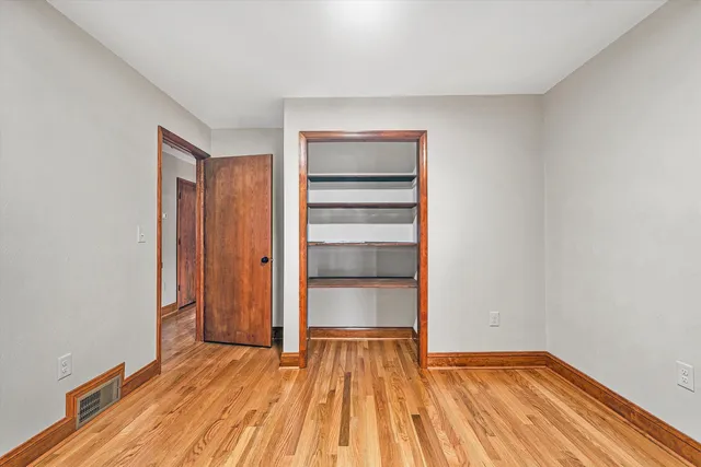 an empty room with a chandelier fan and wooden floor