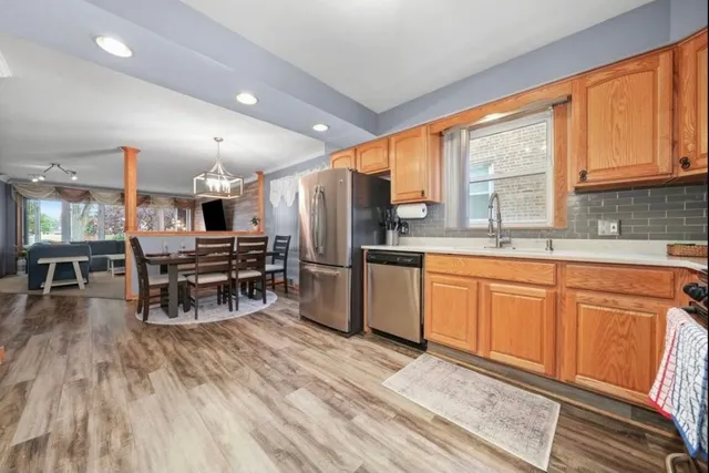 a kitchen with stainless steel appliances kitchen island granite countertop a stove top oven a sink dishwasher a dining table and chairs with wooden floor