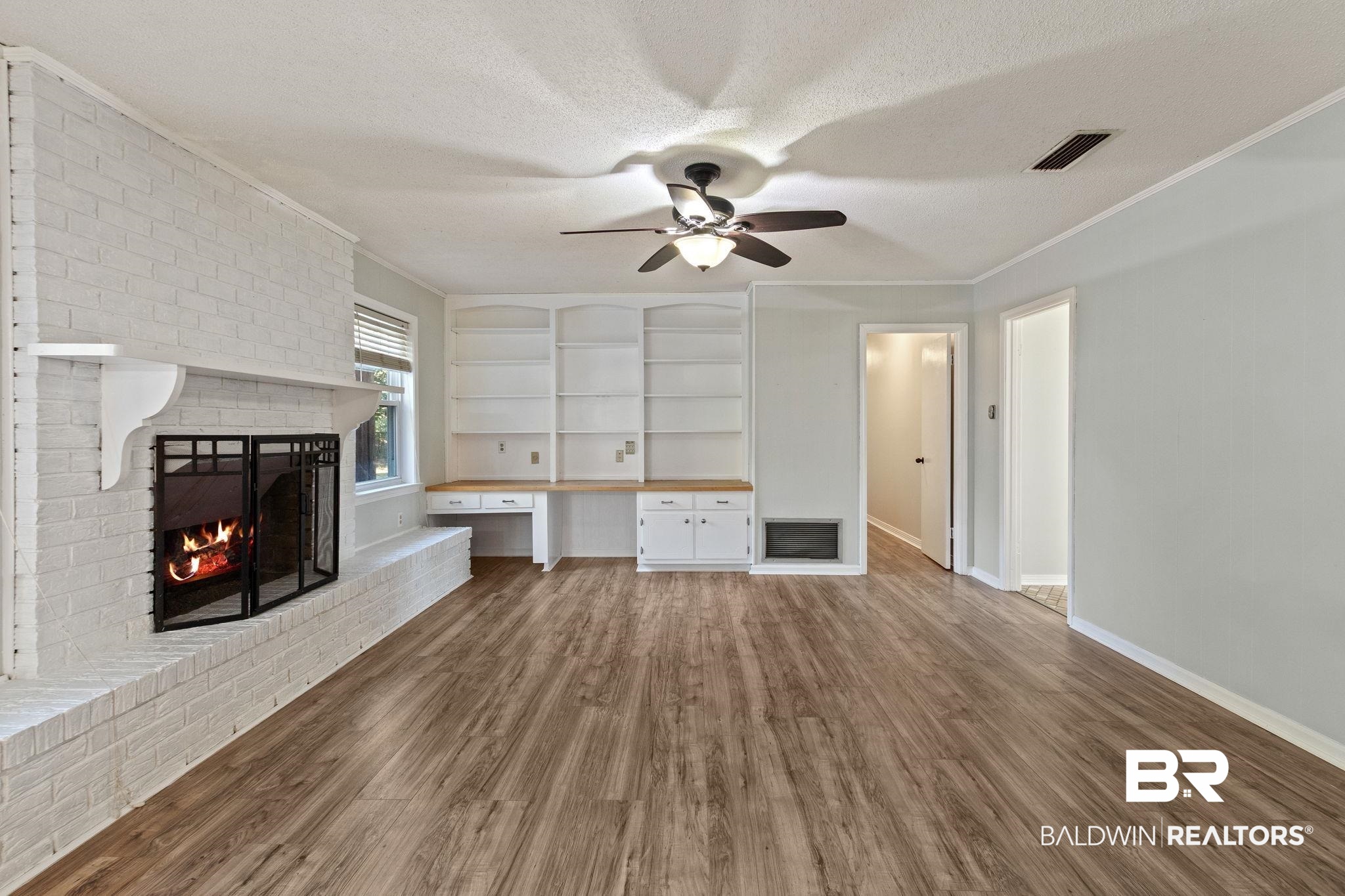 3864 Leroy Stevens Road Mobile, AL 36619 - Photo 5 of 33 Unfurnished living room featuring built in study area, a brick fireplace, crown molding, dark wood-style floors, and built in shelves