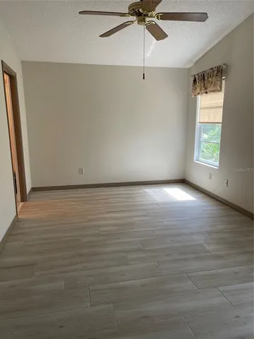 an empty room with wooden floor fan and windows