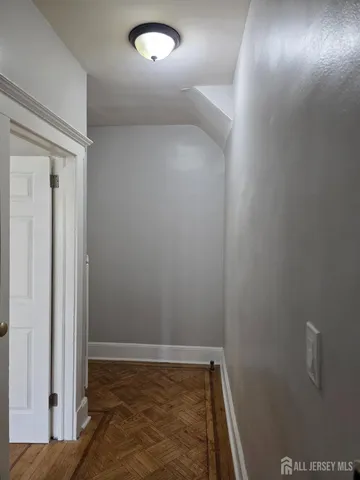 a view of empty room with wooden floor and kitchen