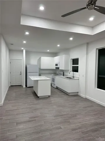 a large room with kitchen island a sink dishwasher stove and white cabinets with wooden floor