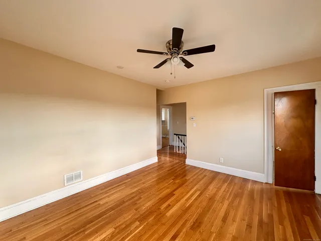 a view of empty room with wooden floor and fan