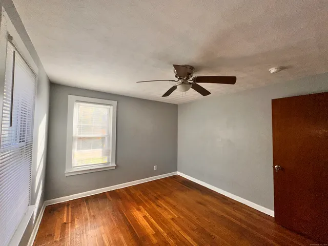 an empty room with wooden floor fan and windows