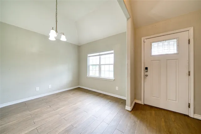 an empty room with wooden floor chandelier and windows