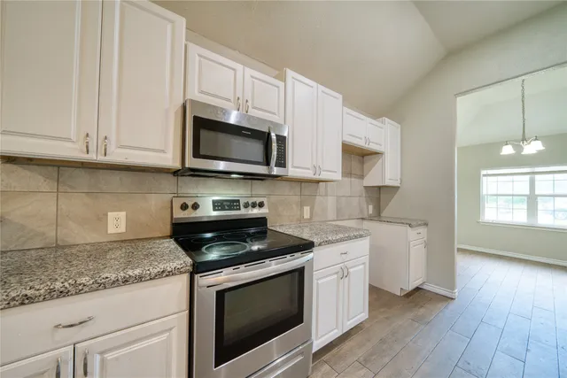 a kitchen with stainless steel appliances granite countertop white cabinets a sink a stove a microwave and dishwasher