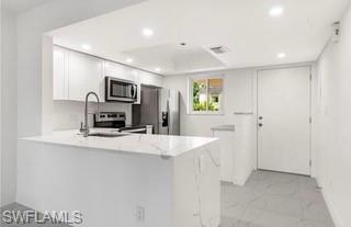 1018 Manatee Road, Unit E107 Naples, FL 34114 - Photo 3 of 15 Kitchen featuring a peninsula, white cabinetry, appliances with stainless steel finishes, recessed lighting, and light stone countertops